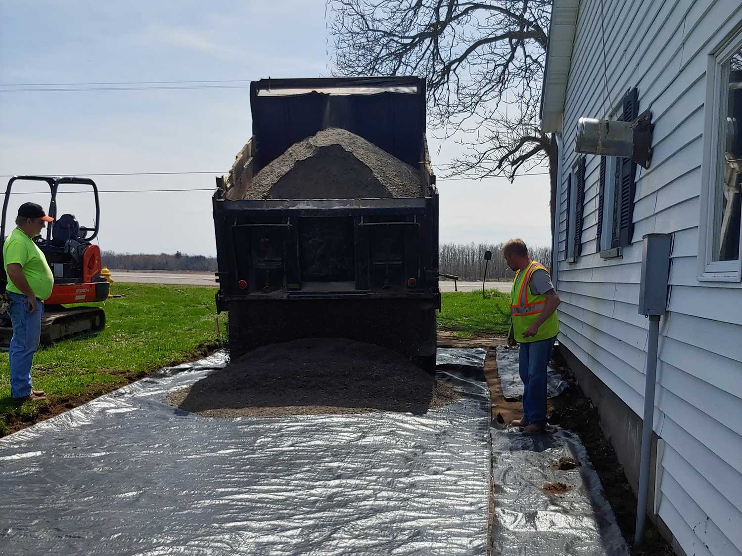 black dump truck unloading gravel at the side of a house