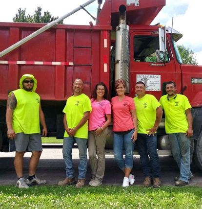 4 men in yellow work shirts and 2 women in pink work shirts standing beside red dump truck during daytime