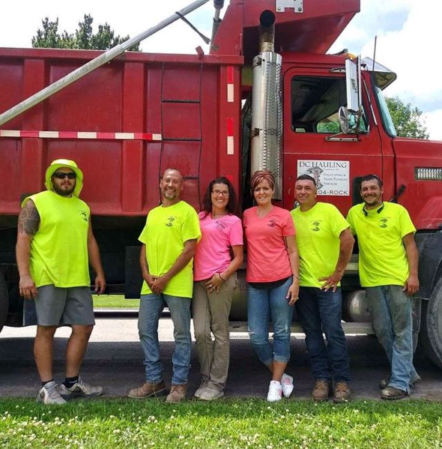 4 men in yellow work shirts and 2 women in pink work shirts standing beside red dump truck during daytime