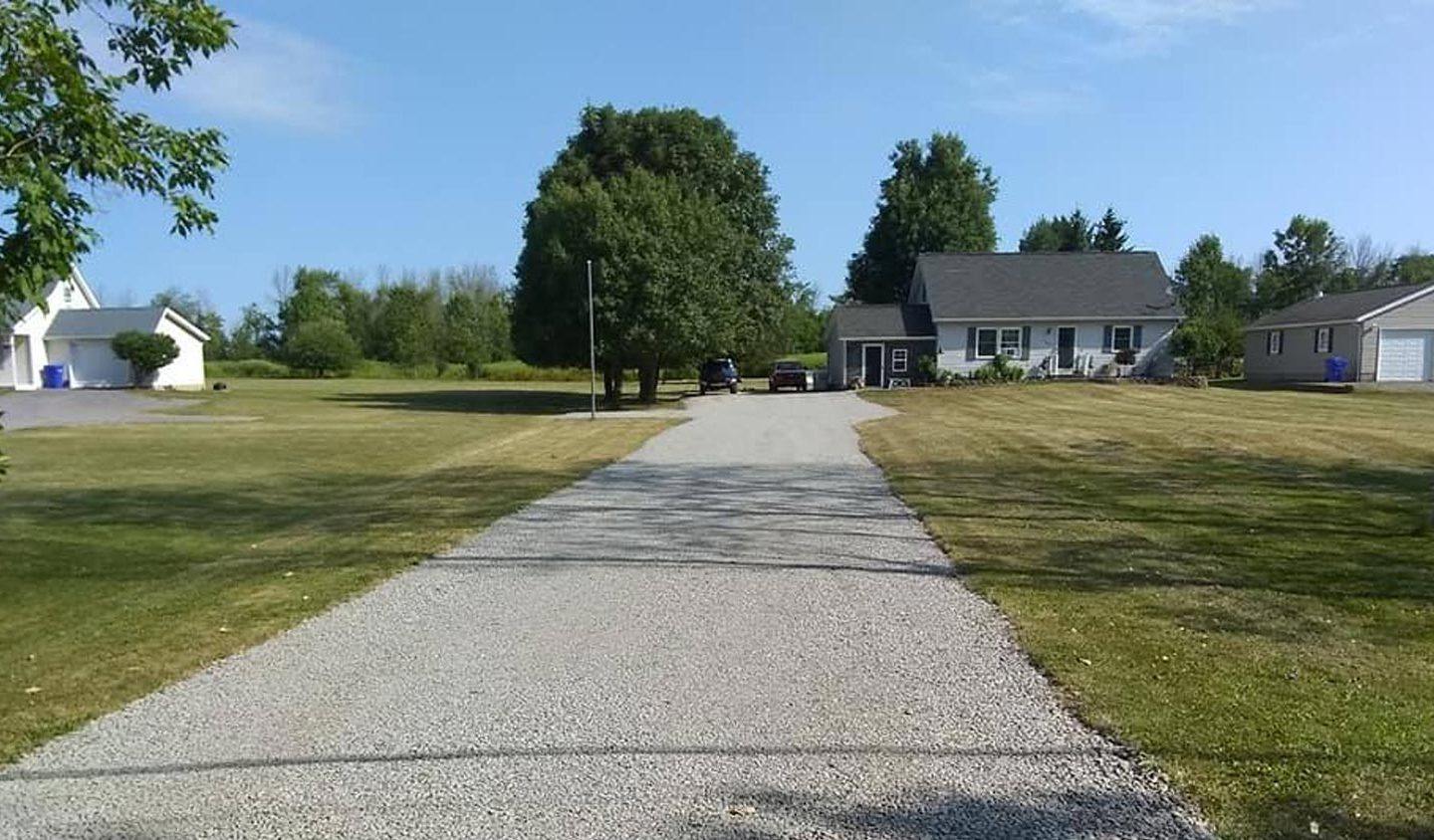 grey gravel driveway between green grass during daytime