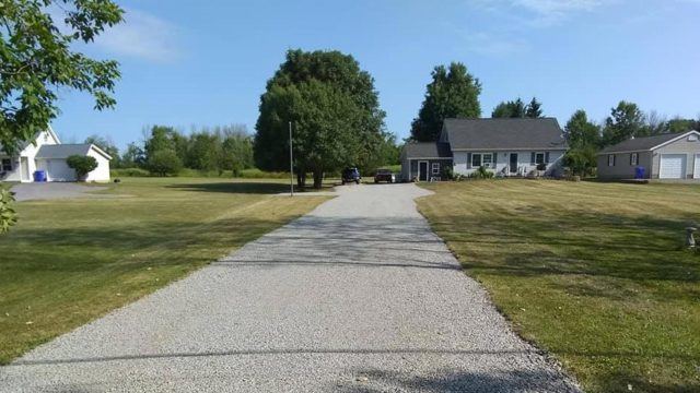 grey gravel driveway between green grass during daytime