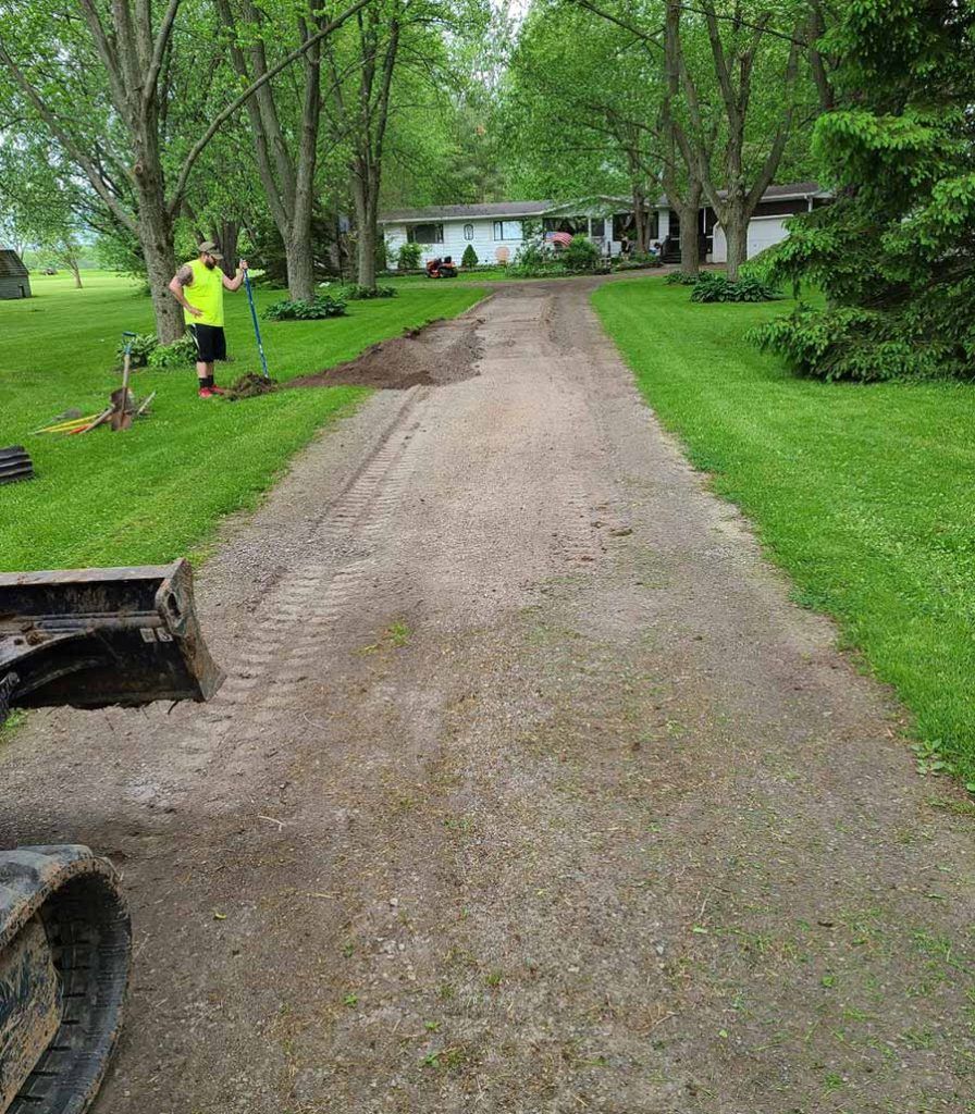 a man working outside with a rake working on a gravel driveway