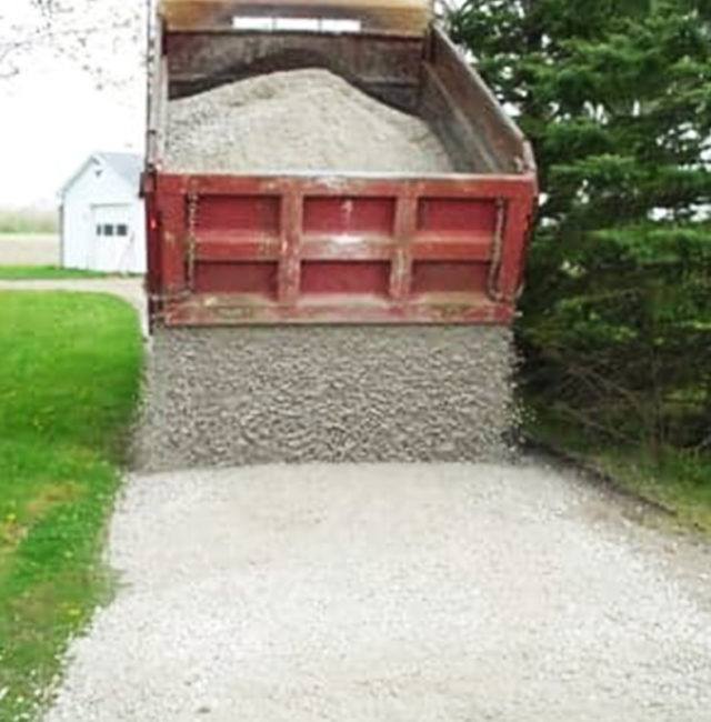 red dump truck unloading gravel onto a driveway